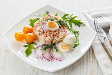 Tuna salad with rice, arugula and tomatoes on light wooden background. Healthy food, seafood menu,