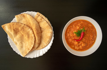 Famous traditional Arabic cuisine - peeled fava beans with chili in white bowl and pita bread on dark wooden background. Top view. Foul Mudammas, egyptian beans, flat bread