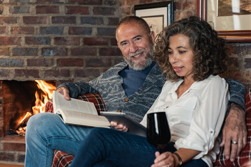 older couple reading by the fireplace drinking wine