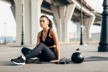 Woman in sportswear resting on mat after workout on city street