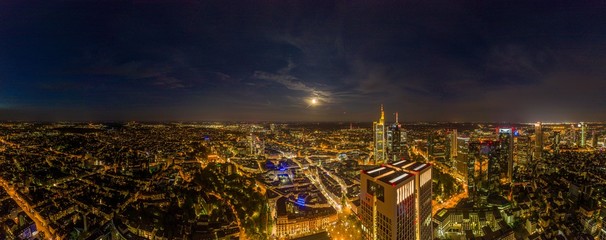 Aerial drone panorama of Frankfurt skyline at night with full moon and illuminated skyscrapers