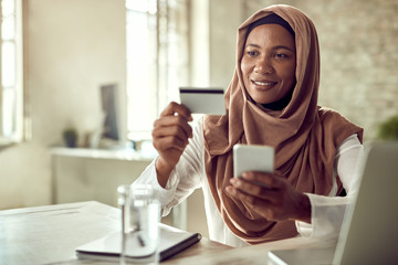 Smiling Islamic businesswoman e-banking over smart phone in the office.