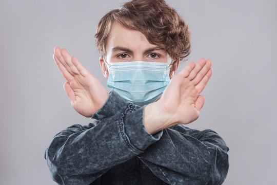 Concept of coronavirus quarantine. Child wearing medical protective mask during flu virus, making stop gesture. COVID-19. Student teen Boy doing stop sign with crossed hands, on grey background.