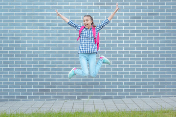 Fototapeta na wymiar Happy schoolchild with backpack jumping against a brick wall outdoors. Cheerful cute child pupil Teen Girl Back to School. Concepts of freedom, childhood and education.