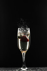 Red strawberry drops in a glass of champagne on a black background. Spray flying to the sides.