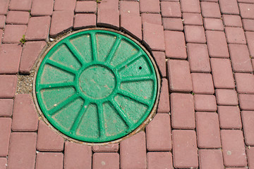 A manhole with radial ribs is built into red paving stones.