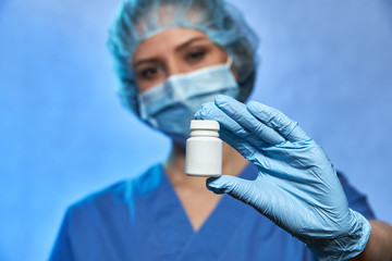 White bottle with pills on foreground in hand in glove of blurred doctor in medical mask and cap on background, Coronavirus COVID-19