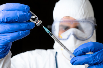 Doctor or scientist in PPE suite uniform in lab hold medicine liquid vaccine vial bottle and syringe on black isolated background .