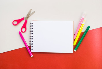 Colorful box with pencils, markers and scissors and a notebook on white and red background with copyspace. 2020 color trend. Back to school concept.