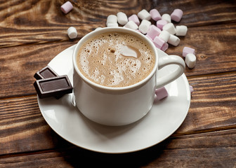 the cap of coffee on a small plate with two small chocolate and marshmallow on the table.  