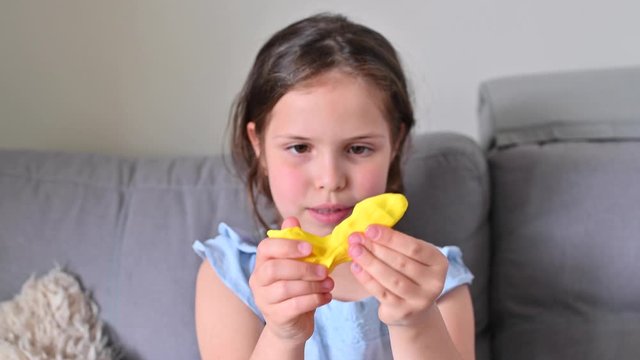 Little girl is playing with yellow plasticine. Clay for modeling in the hands of a child. Games and creativity at home for development. Game process.