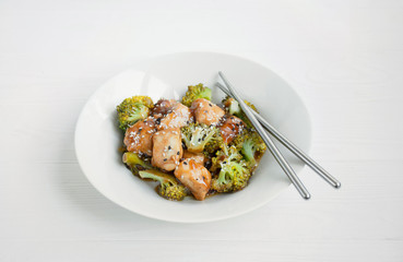 Salad with broccoli and chicken. Hot salad in the sauce served in a white plate. Asian style dish. Light background.