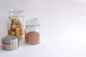 Glass jars with cane sugar and cocoa on a white background, close-up, selective focus, space for your text. The concept of the desserts
