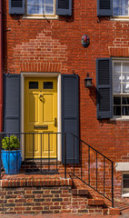 Fototapeta na wymiar Old house in Annapolis Maryland with elegant yellow door with protective shutter, orange brick walls, steps leading to the door with black railings