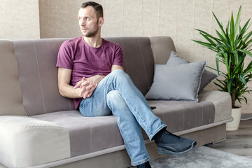 Obraz premium young calm man sits on a sofa in a bright room and looks out the window