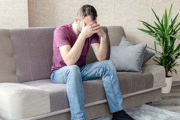 young sad man sitting on a sofa in a bright room