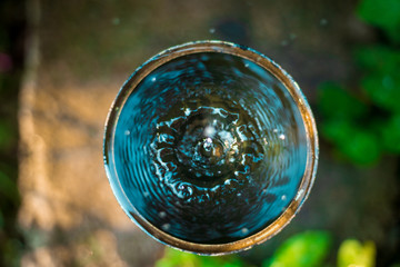 Top view of water leaking from a tap into round container outdoors garden. selective focus