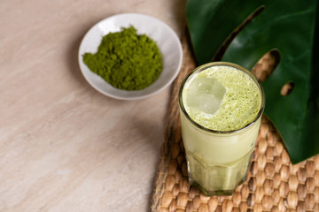 Glasses of matcha latte with coconut milk and white chocolate on marble background. Tropical monstera leaf