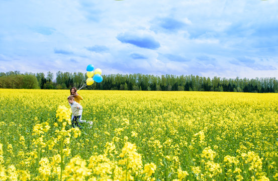 happy two children run on a yellow field, blooming rapeseed. blue sky and clouds. Blue and yellow balloons, concept of freedom, summer. Holiday and birthday. Central Europe