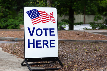 Vote here sign with an American flag and no hours to vote for elected government officials.