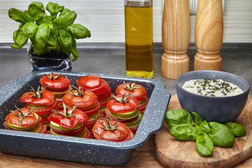 Baked tomatoes and zucchini with basil and sour cream sauce in a baking dish
