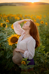 Beautiful red-haired girl with gray eyes walks in a summer sunflower field © Maria