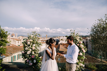 Destination fine-art wedding in Florence, Italy. Multiracial wedding couple. A wedding ceremony on the roof of the building, with cityscape views of the city and the Cathedral of Santa Maria Del Fiore