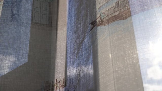 Sun shining through an open window with transparent curtain moved by the wind on a sunny clear day.
