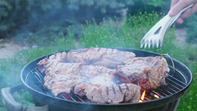 Man cooking meat on black round barbecue grill bbq rotating beaf steaks with open fire smoke