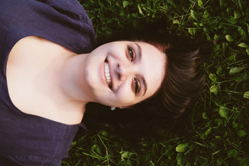 Happy smiling caucasian young woman lying on grass, top view. Copy space. Close-up outdoors portrait of plus size model with cute smile spending time in nature. Summer recreation concept.