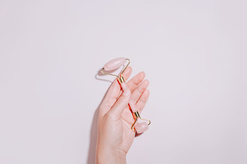 Hand holding facial roller, gua sha on pink. Natural cosmetics and facial tools on pastel...