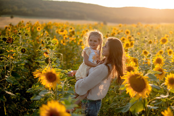 Beautiful mother and daughter walk and hug in a sunflower field in summer