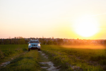 Obraz na płótnie Canvas white suv car at field road on sunset
