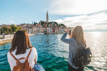woman traveler looking at rovinj city from the harbour taking picture on the phone
