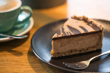 Slice of vegan peanut butter cake in cafe. Green cup with coffee cappuccino