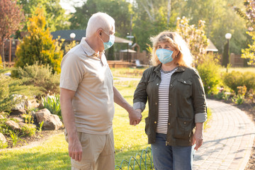 Happy elderly seniors couple wearing medical mask to protect from coronavirus in summer park