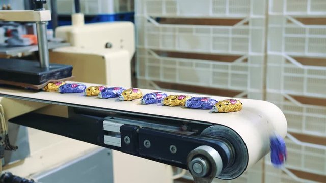 Candy factory. Wrapped candies lying on conveyor. Tasty sweets lying on conveyor during wrapping process on industrial machine in confectionery factory.