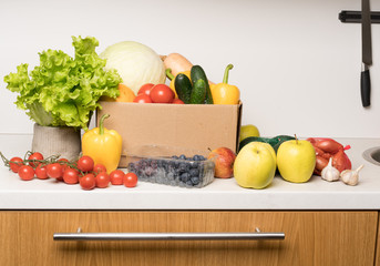 groceries box with vegetables and fruits on white kitchen background. Food delivery services during coronavirus pandemic and social distancing. Shopping online.