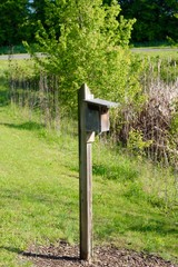 The old wooden box birdhouse on the post in the grass.