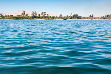 Fototapeta premium Surface of Nile river with palm trees on shore and chalk stone dunes at background