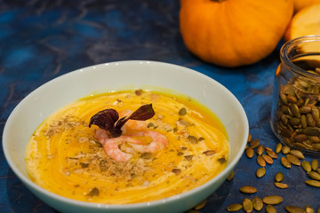 Tasty pumpkin cream soup with shrimps and basil leaves