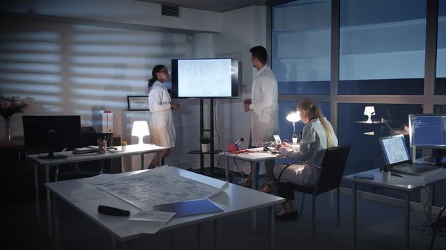 Team of Computer Engineers discussing something on a big TV screen in lab. They explaining details of research