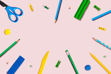 Pink background with writing materials. Back to school flat lay with colored pencils, scissors, plasticine, and paper clips.