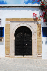 Traditional Tunisian black metal door with a pattern on a white wall with stone platbands. Sidi Bou Said, Tunisia