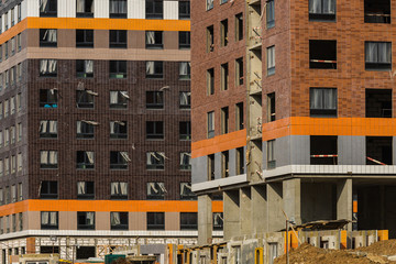 Obraz premium Construction of a new residential complex for young families. Concept business, real estate, mortgage. Sunny warm day. High multi-storey building with windows.
