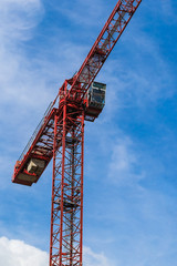 Red tower crane against blue sky with white clouds. Close up. Vertical photo. Copy space.