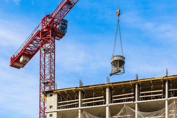 One high-rise crane with concrete mixer against a house and sky during the construction phase....