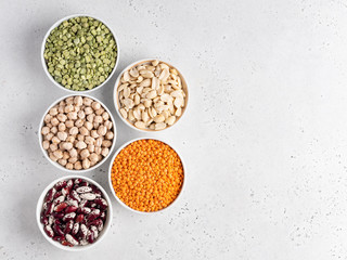 Obraz na płótnie Canvas Legumes assortment. Red lentils, dried green peas, chickpeas, red kidney beans in white ceramic bowls on wooden tray. Natural and vegetarian protein food. Copy space. Top view. Concrete background.