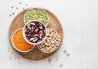 Legumes assortment. Red lentils, dried green peas, chickpeas, red kidney beans in white ceramic bowls on wooden tray. Natural and vegetarian protein food. Copy space. Top view. Concrete background.