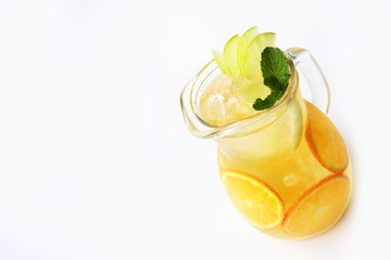 Lemonade of oranges and apples with mint in a tall glass jug on a white background. An isolated object.